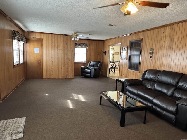 living area featuring a textured ceiling, ceiling fan, ornamental molding, and wooden walls