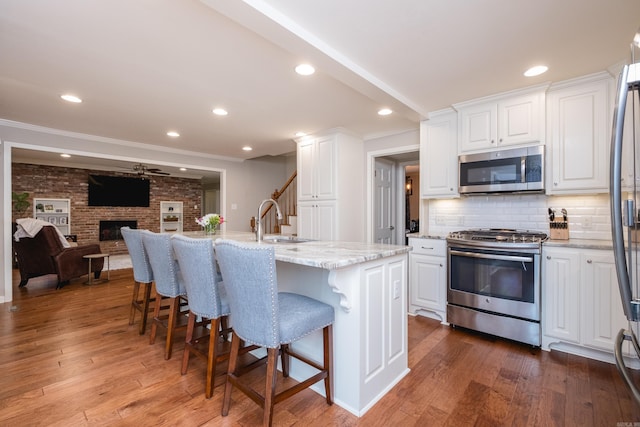 kitchen featuring a fireplace, wood-type flooring, appliances with stainless steel finishes, white cabinetry, and a sink