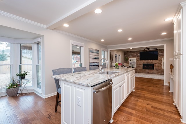 kitchen with a fireplace, stainless steel dishwasher, light wood-style floors, ornamental molding, and a kitchen bar