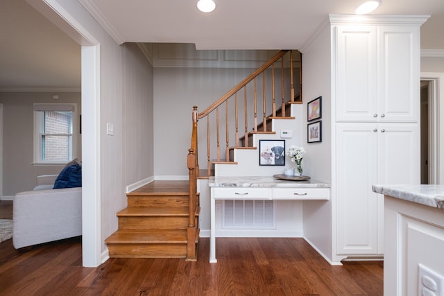 stairs with baseboards, built in desk, wood finished floors, and crown molding