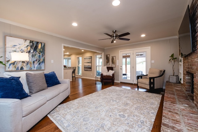 living room featuring ceiling fan, a fireplace, wood finished floors, and crown molding