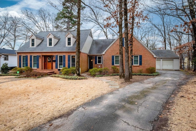 cape cod house featuring a garage, driveway, an outdoor structure, and brick siding