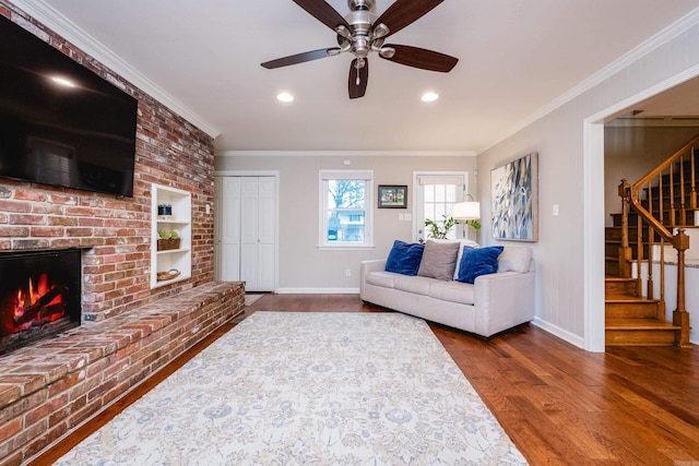 living area featuring baseboards, stairway, wood finished floors, crown molding, and a brick fireplace