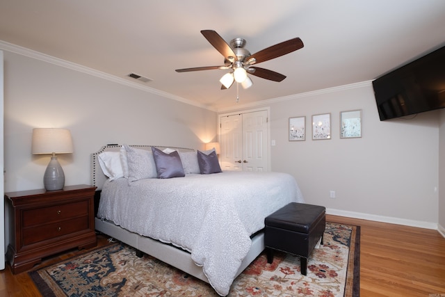 bedroom with crown molding, a closet, visible vents, wood finished floors, and baseboards