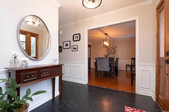 hallway with a wainscoted wall, crown molding, dark tile patterned floors, and a decorative wall