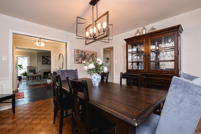 dining space with a chandelier, a decorative wall, a fireplace, wainscoting, and crown molding