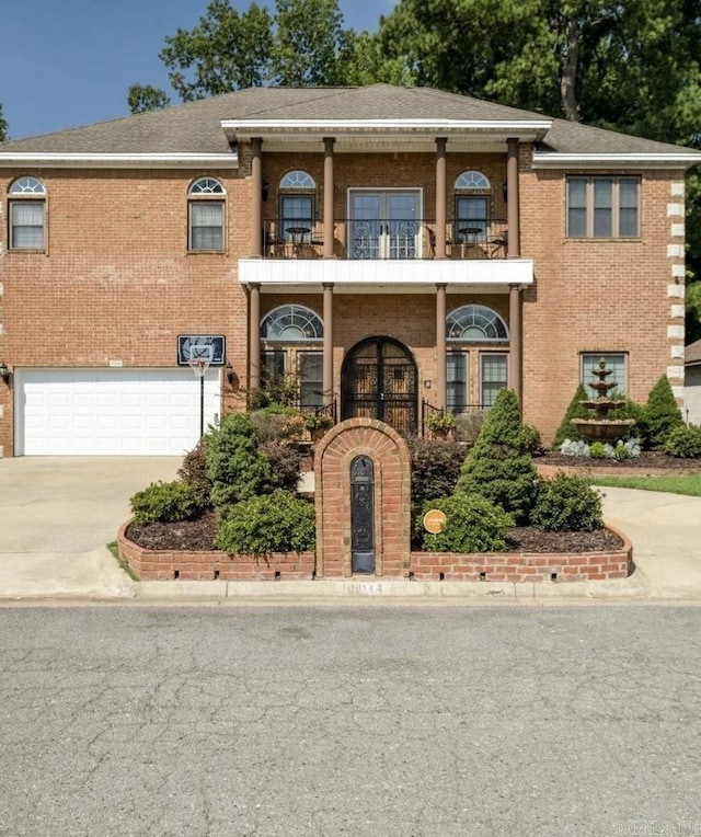 view of front of home featuring driveway, a garage, a balcony, roof with shingles, and brick siding