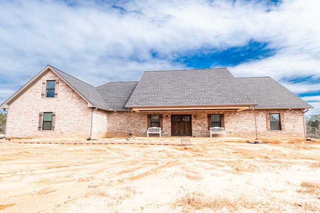 view of front of property featuring brick siding and roof with shingles