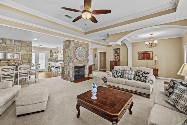 living area with baseboards, visible vents, a tray ceiling, crown molding, and a stone fireplace