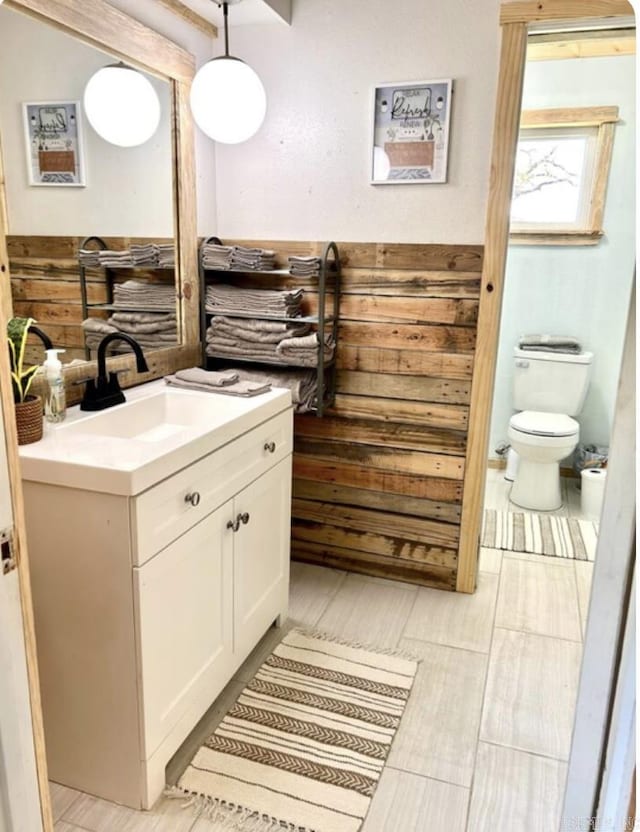 bathroom featuring wood walls, vanity, and toilet