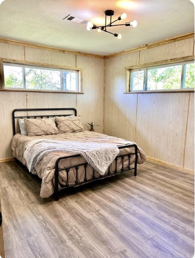 bedroom with multiple windows, a notable chandelier, wooden walls, and wood finished floors