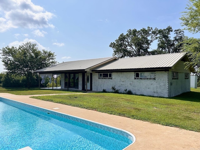 rear view of property with metal roof, brick siding, a lawn, and an outdoor pool