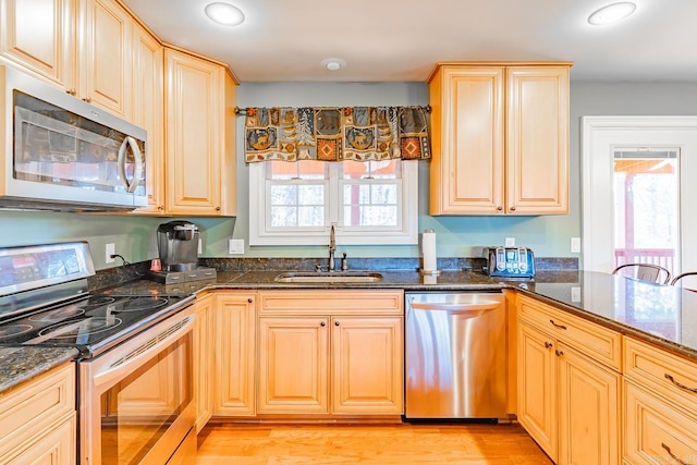 kitchen featuring dark stone counters, appliances with stainless steel finishes, light wood-type flooring, and a sink