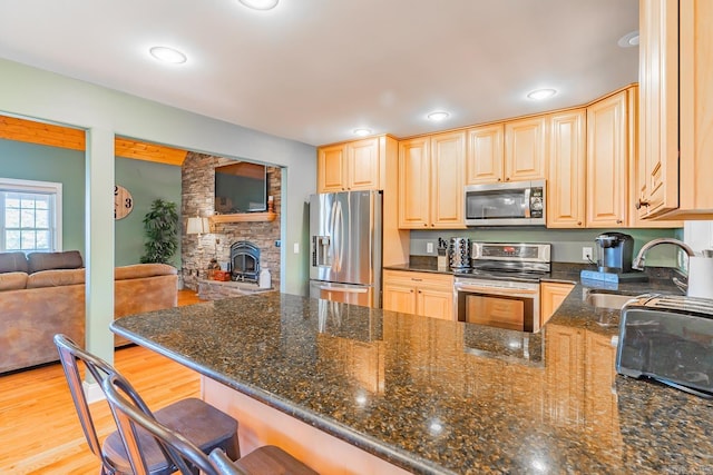 kitchen featuring open floor plan, appliances with stainless steel finishes, dark stone countertops, and a kitchen bar