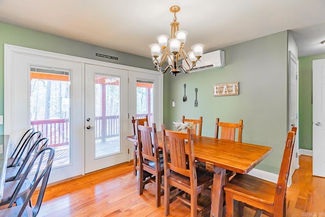 dining room featuring light wood finished floors, baseboards, a wall mounted air conditioner, french doors, and a chandelier