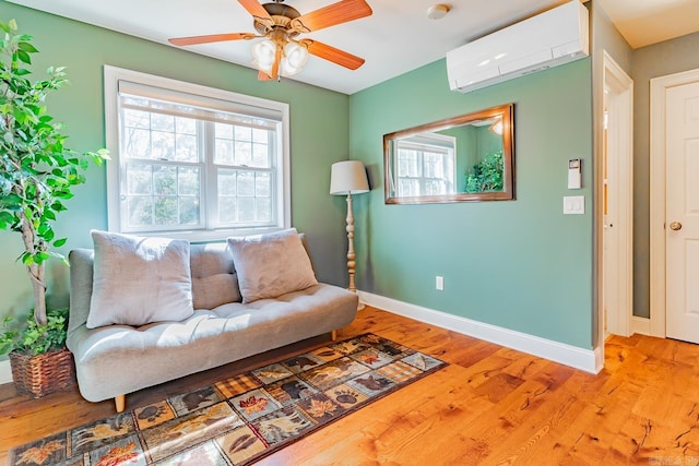 living area with light wood-type flooring, ceiling fan, baseboards, and a wall mounted air conditioner