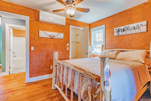 bedroom with an AC wall unit, ensuite bathroom, baseboards, and wood finished floors