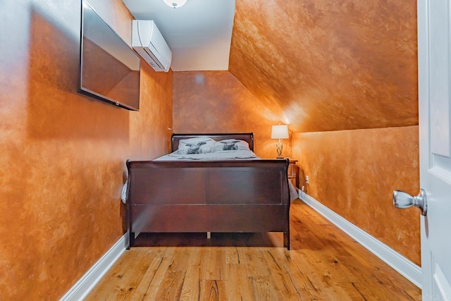 bedroom featuring baseboards, a wall unit AC, and light wood finished floors