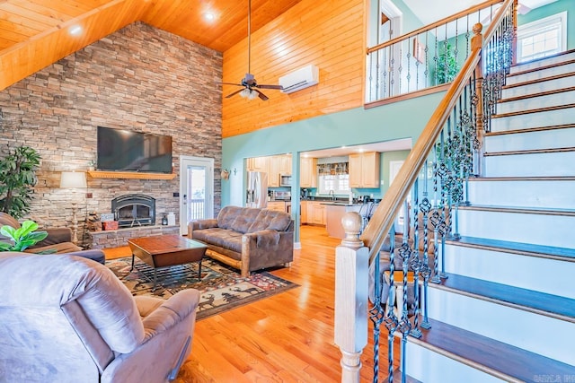 living room featuring light wood finished floors, stairway, a wall mounted air conditioner, a stone fireplace, and a wealth of natural light