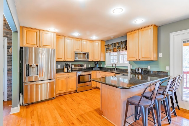 kitchen featuring dark stone counters, a breakfast bar, a peninsula, stainless steel appliances, and a sink