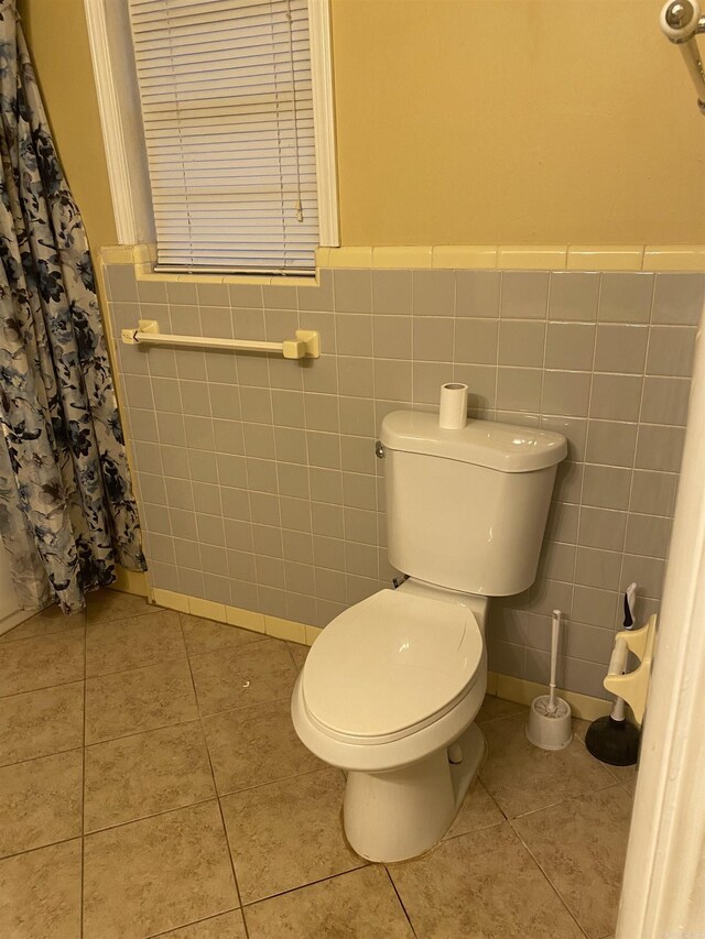 bathroom with toilet, a wainscoted wall, tile walls, and tile patterned floors