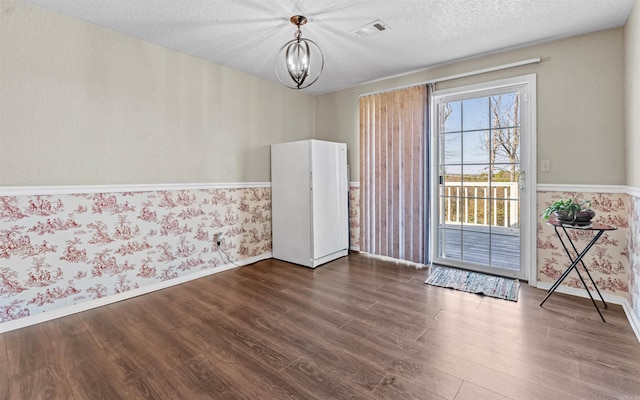 interior space featuring wallpapered walls, visible vents, dark wood-style flooring, a textured ceiling, and a chandelier