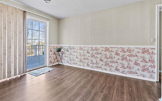 doorway with dark wood-style flooring, a textured ceiling, baseboards, and wallpapered walls