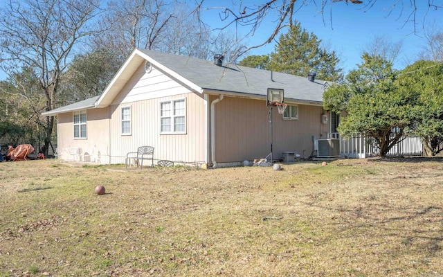 view of side of home with central AC unit, fence, and a lawn