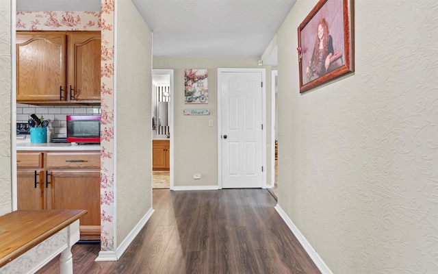 hallway with a textured ceiling, a textured wall, dark wood-type flooring, and baseboards