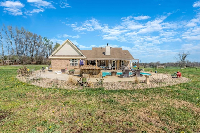 back of property with a chimney, an outdoor pool, a lawn, and a patio