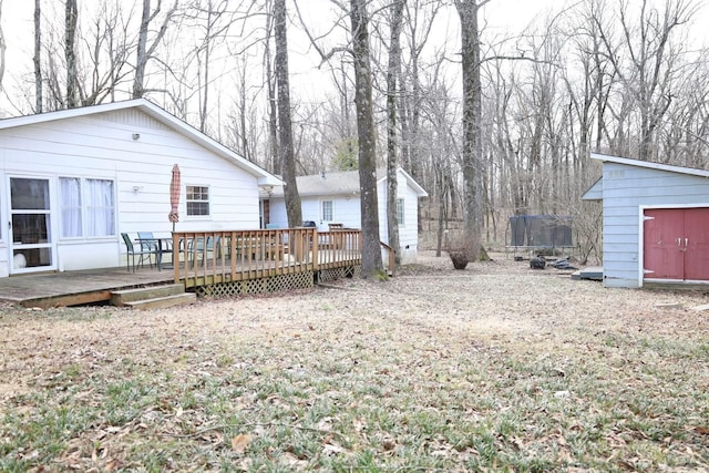 rear view of property featuring a shed, a trampoline, an outdoor structure, and a wooden deck