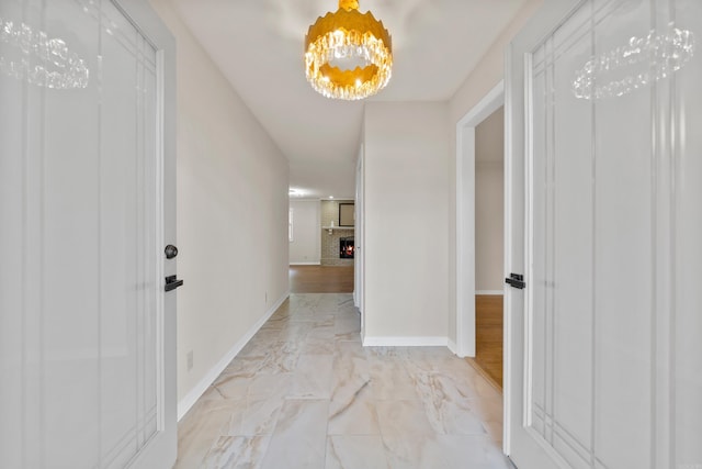 hallway with marble finish floor, a notable chandelier, and baseboards