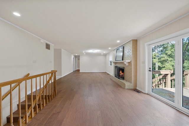 unfurnished living room featuring a brick fireplace, wood finished floors, visible vents, and crown molding