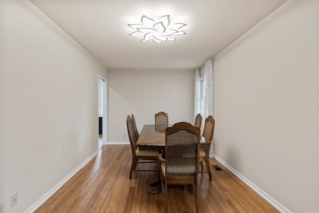 dining space featuring light wood-type flooring, visible vents, and baseboards