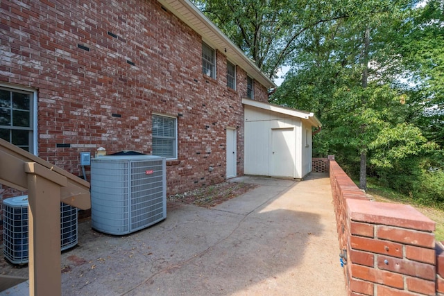 exterior space with a storage unit, central AC unit, an outbuilding, and brick siding