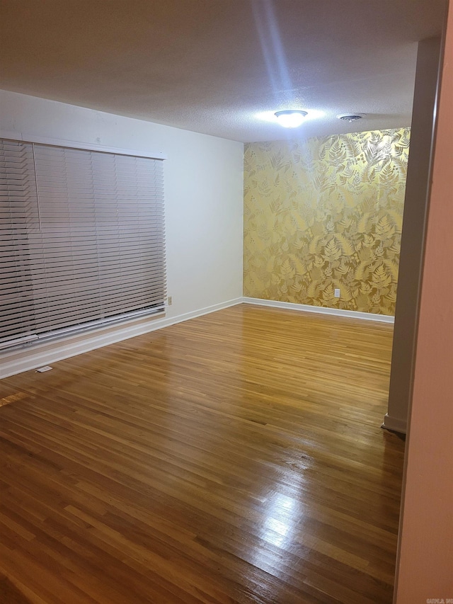 empty room featuring baseboards, a textured ceiling, wood finished floors, and wallpapered walls