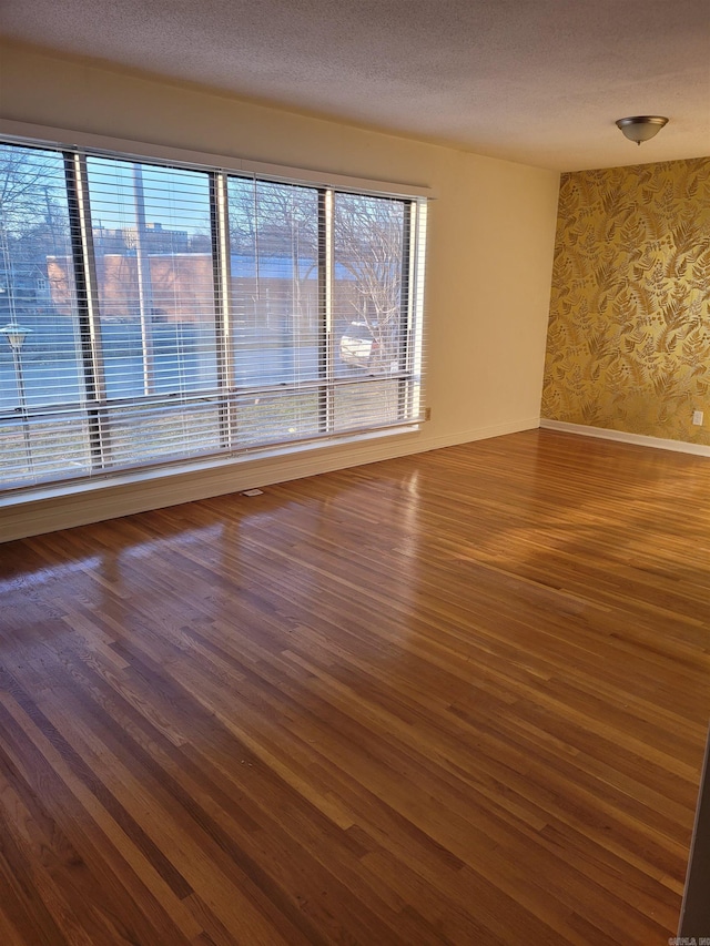 unfurnished room with wallpapered walls, baseboards, dark wood-style floors, and a textured ceiling