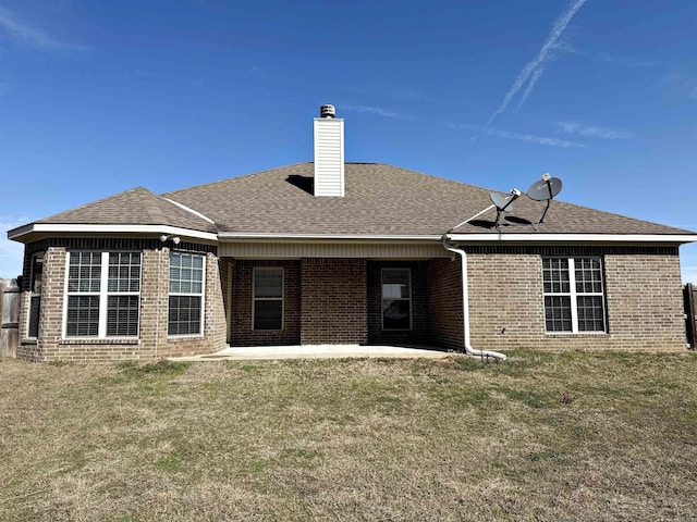 rear view of house with brick siding, a yard, a chimney, a shingled roof, and a patio area