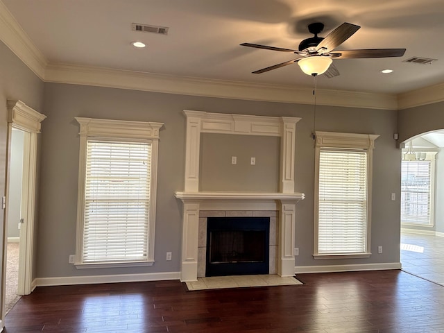 unfurnished living room featuring dark wood-style flooring, crown molding, a fireplace, visible vents, and baseboards