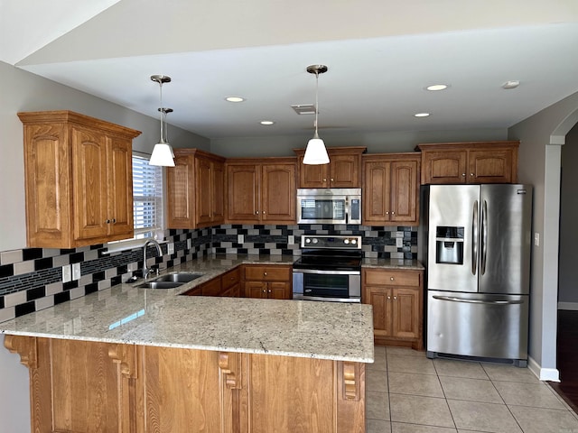 kitchen featuring appliances with stainless steel finishes, a peninsula, light stone countertops, hanging light fixtures, and a sink