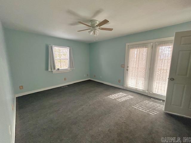 empty room featuring visible vents, dark carpet, baseboards, and ceiling fan