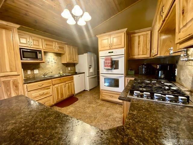 kitchen with white appliances, decorative backsplash, lofted ceiling, an inviting chandelier, and a sink