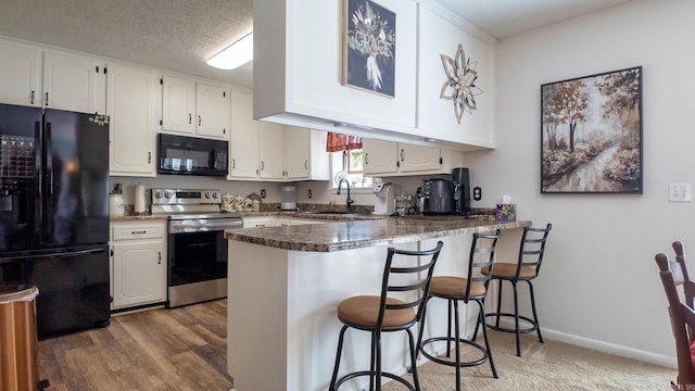 kitchen featuring dark countertops, a kitchen breakfast bar, a peninsula, black appliances, and white cabinetry