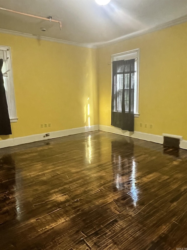 empty room with ornamental molding, visible vents, baseboards, and dark wood-style floors