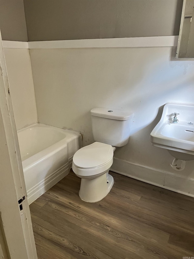 bathroom with toilet, a tub, a sink, and wood finished floors