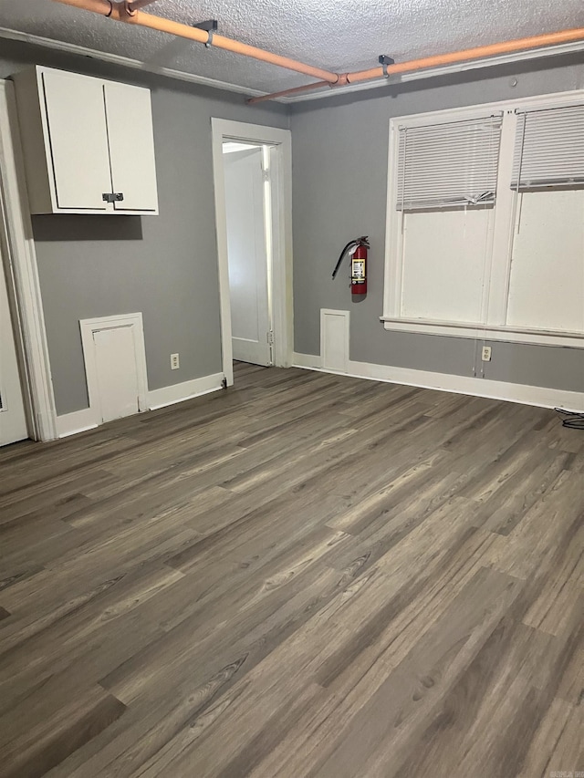 empty room with a textured ceiling, baseboards, and dark wood-type flooring