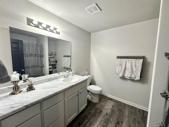 full bathroom with visible vents, toilet, vanity, a textured ceiling, and wood finished floors