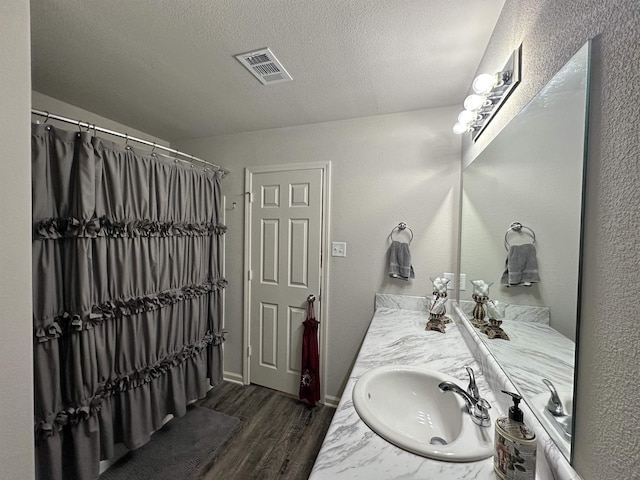 full bath with baseboards, visible vents, wood finished floors, a textured ceiling, and vanity