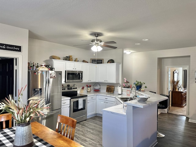 kitchen with a peninsula, a sink, white cabinets, light countertops, and appliances with stainless steel finishes