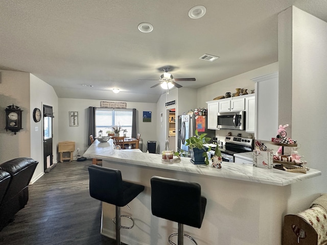 kitchen with visible vents, appliances with stainless steel finishes, white cabinetry, a peninsula, and a kitchen bar